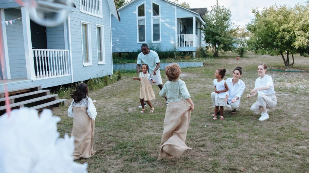 Children and adults have fun with a lively sack race outside a cozy home on a sunny day.